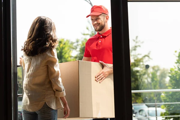 Cheerful delivery man in cap holding box near woman — Stock Photo