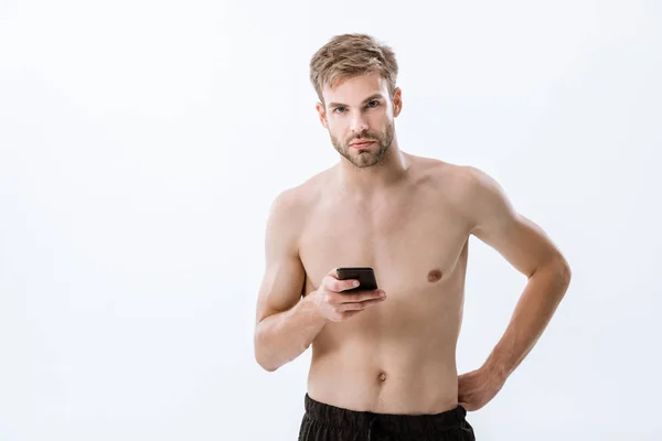 Deportista sin camisa barbuda mirando a la cámara y sosteniendo el teléfono inteligente aislado en gris - foto de stock