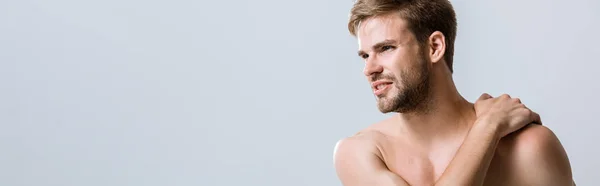 Panoramic shot of shirtless bearded man with pain in shoulder isolated on grey — Stock Photo