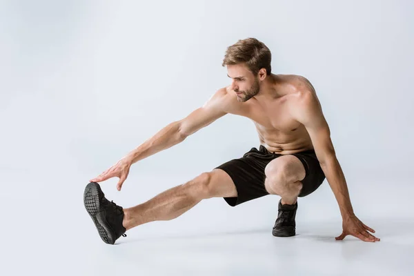 Uomo barbuto senza maglietta in scarpe da ginnastica nere che si estende sul grigio — Foto stock