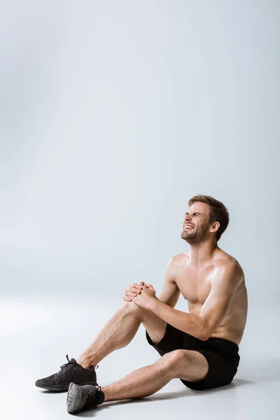 Бородатый мужчина без рубашки с болью в колене на сером — стоковое фото