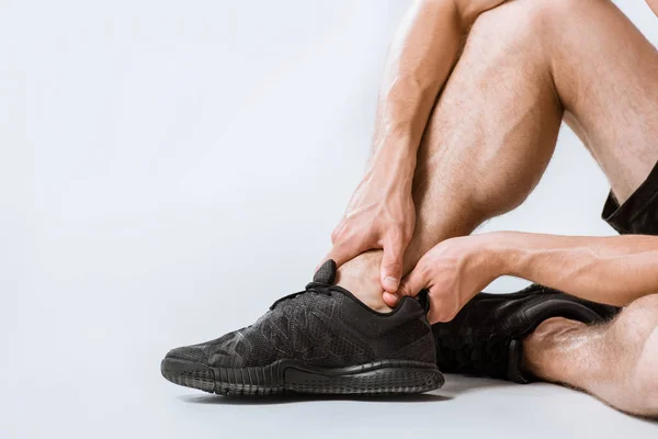 Vue partielle du sportif avec douleur à la cheville sur fond gris — Photo de stock