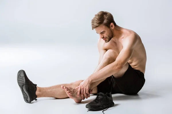 Shirtless bearded sportsman with ankle pain on grey — Stock Photo