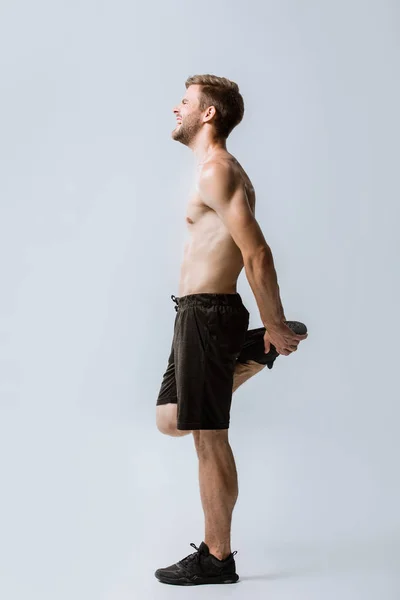 Full length view of shirtless sportsman feeling pain while warming up on grey — Stock Photo