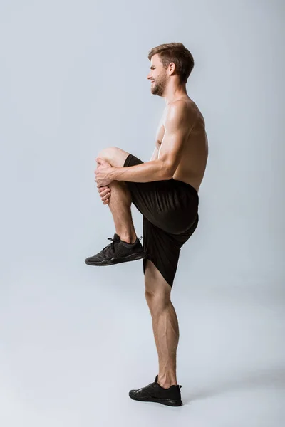 Вигляд на повну довжину без сорочки спортсмен відчуває біль під час прогрівання на сірому — стокове фото