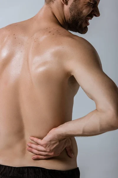 Обрезанный вид спортсмена без рубашки с болью в пояснице, изолированный на сером — стоковое фото
