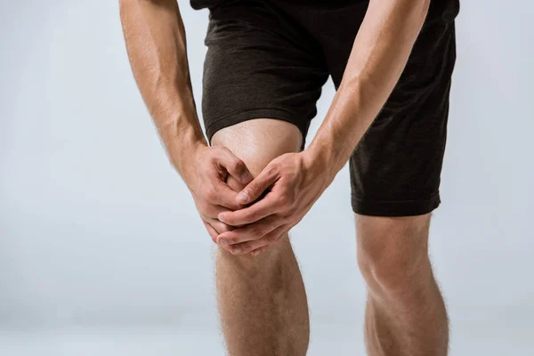 Cropped view of sportsman with knee pain isolated on grey — Stock Photo