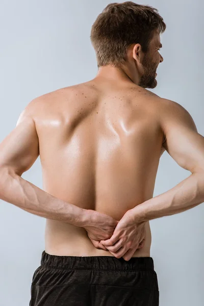 Back view of shirtless sportsman with lower back pain isolated on grey — Stock Photo