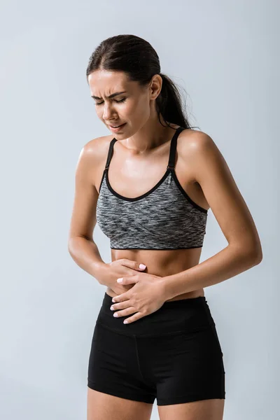 Attractive sportswoman with stomach pain isolated on grey — Stock Photo
