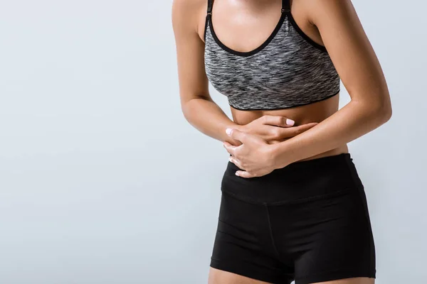 Partial view of sportswoman with stomach pain isolated on grey — Stock Photo