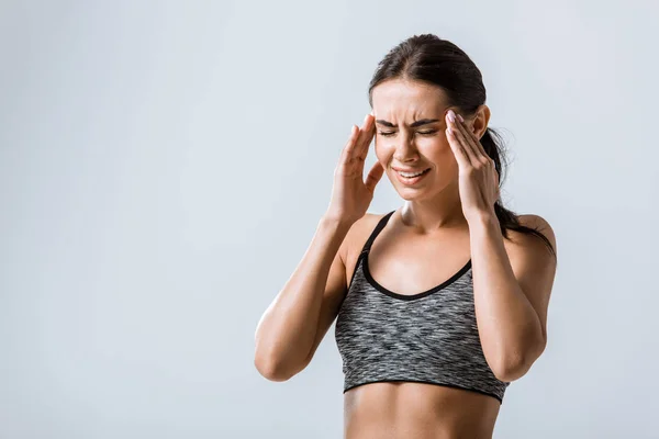 Attractive sportswoman with headache touching temples isolated on grey — Stock Photo