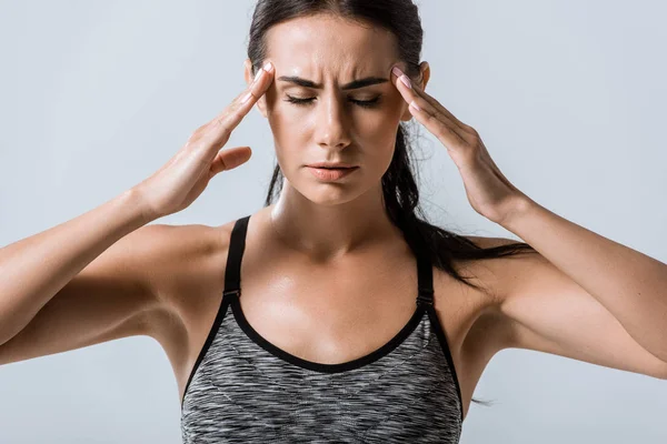 Attractive sportswoman with headache touching temples isolated on grey — Stock Photo