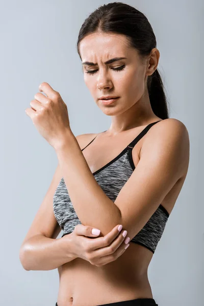 Attraktive Sportlerin mit Ellbogenschmerzen isoliert auf grau — Stockfoto