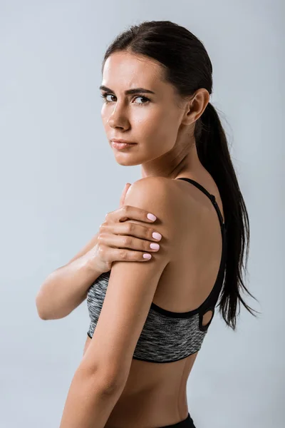 Attractive brunette sportswoman with arm pain isolated on grey — Stock Photo