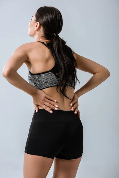 Back view of sportswoman with lower back pain isolated on grey — Stock Photo