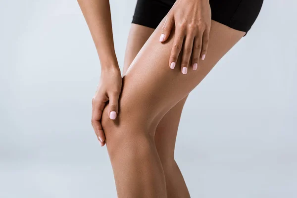 Обрезанный вид спортсменки с болью в колене, изолированный на сером — стоковое фото