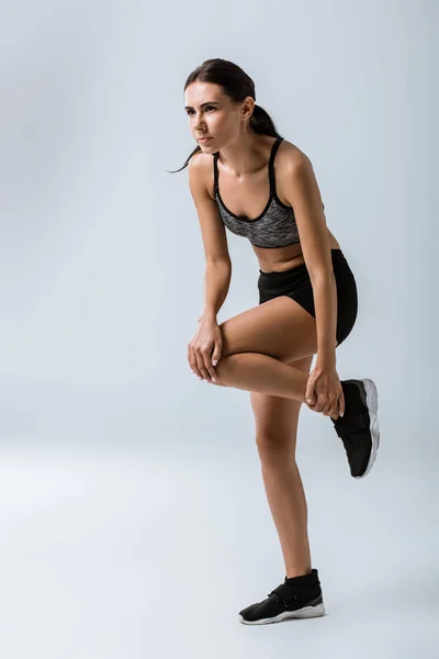 Vue pleine longueur de la sportive ressentant une douleur au genou tout en s'échauffant sur gris — Photo de stock