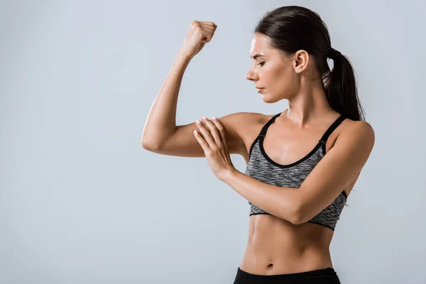 Attraente bruna sportswoman toccare muscolo isolato su grigio — Foto stock