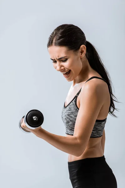 Attractive brunette sportswoman using dumbbell isolated on grey — Stock Photo