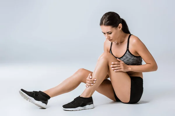 Attractive brunette sportswoman with knee pain on grey — Stock Photo