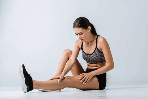 Jolie sportive brune avec douleur aux jambes sur fond gris — Photo de stock