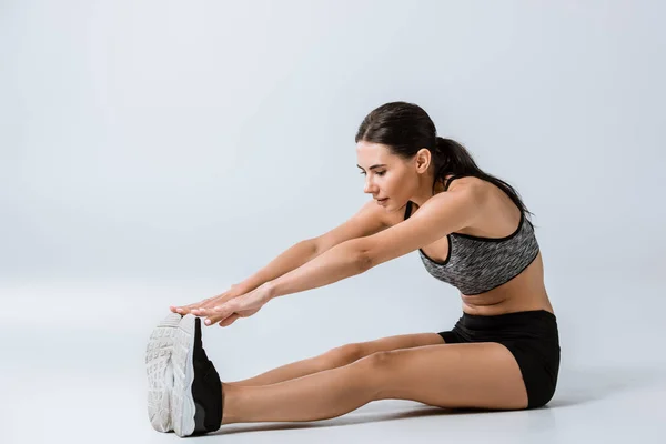 Attractive brunette sportswoman in sportswear stretching on grey — Stock Photo
