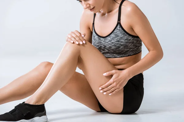 Cropped view of sportswoman with leg pain on grey — Stock Photo