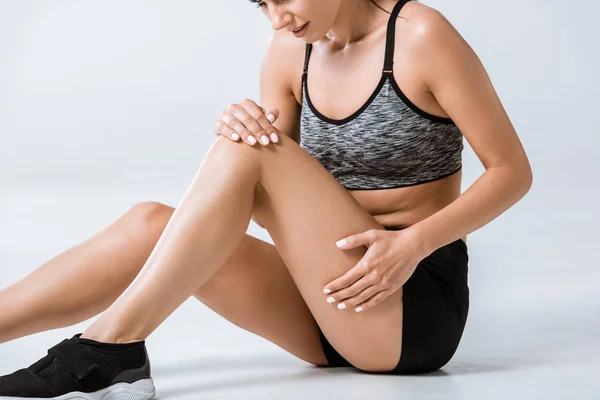 Vue recadrée d'une sportive avec douleur aux jambes sur fond gris — Photo de stock