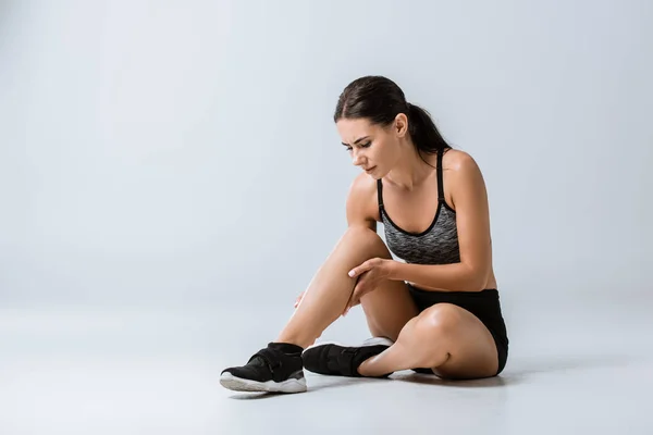 Привлекательная брюнетка спортсменка с болью в ногах на сером — стоковое фото
