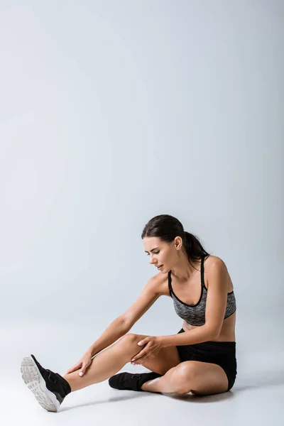 Attractive brunette sportswoman with leg pain on grey — Stock Photo