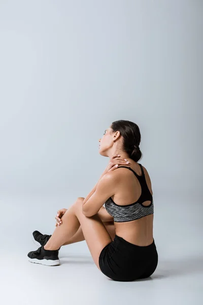 Morena deportista en ropa deportiva con dolor de hombro en gris - foto de stock