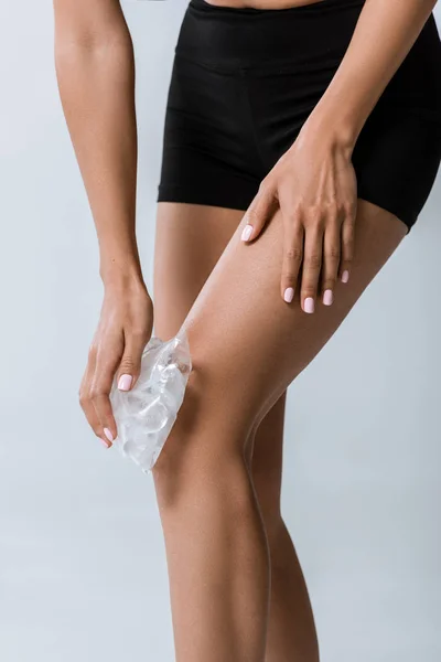 Частковий вид спортсменки, що використовує лід для коліна ізольовано на сірому — стокове фото