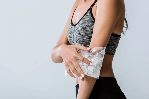 Cropped view of sportswoman using ice for elbow isolated on grey — Stock Photo