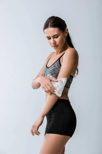 Suffering sportswoman using ice for elbow isolated on grey — Stock Photo