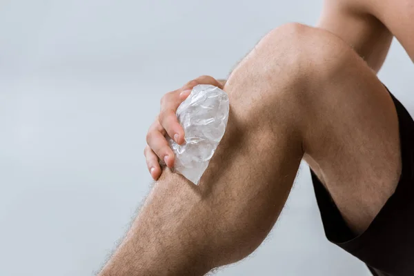 Vista parziale dello sportivo che utilizza ghiaccio per il ginocchio isolato su grigio — Foto stock