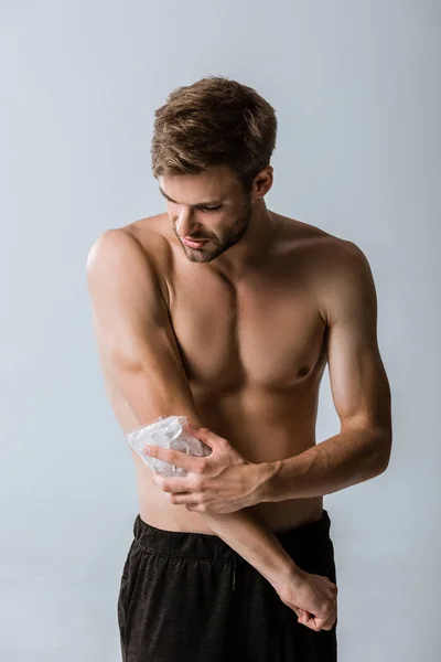 Без сорочки спортсмен використовує лід для ліктя ізольовані на сірому — стокове фото