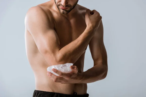 Vue recadrée d'un sportif torse nu utilisant de la glace pour son coude isolé sur du gris — Photo de stock