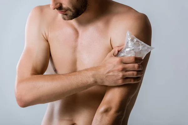 Обрезанный вид человека без рубашки, использующего лед вместо плеча, изолированного на сером — стоковое фото