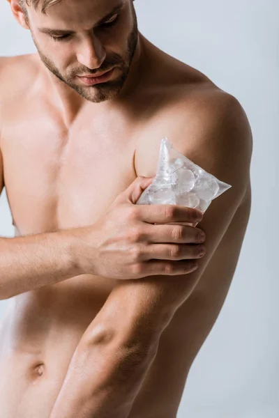 Shirtless man using ice for shoulder isolated on grey — Stock Photo