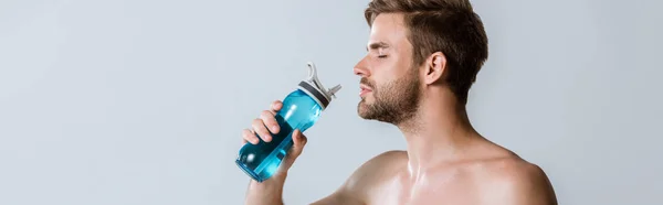 Plano panorámico de un deportista barbudo sin camisa sosteniendo una botella deportiva aislada en gris - foto de stock