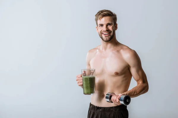 Shirtless sportsman holding smoothie and dumbbell isolated on grey — Stock Photo