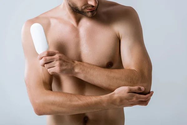 Vue recadrée d'un homme torse nu tenant une bouteille de pommade et touchant le coude isolé sur du gris — Photo de stock