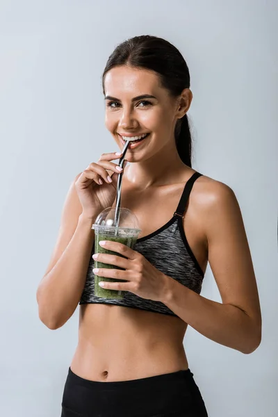 Atraente sorrindo esportista beber smoothie isolado em cinza — Fotografia de Stock