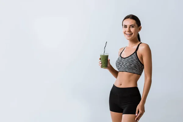 Bela sportswoman sorrindo segurando smoothie isolado em cinza — Fotografia de Stock