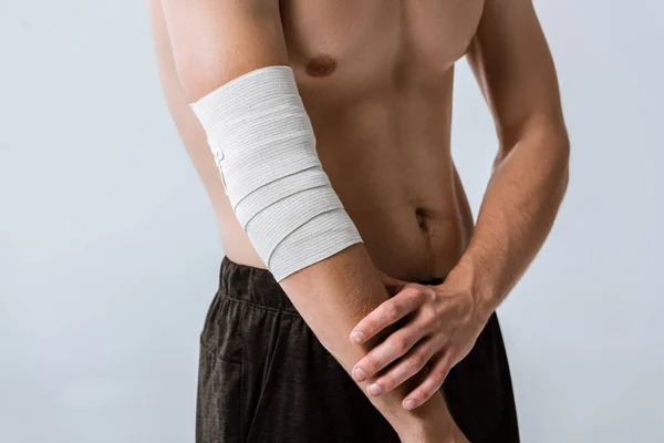 Partial view of shirtless sportsman with elastic bandage on elbow isolated on grey — Stock Photo