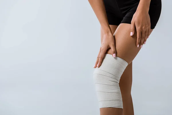 Обрізаний вид спортсменки з еластичною пов'язкою на коліні ізольовано на сірому — стокове фото