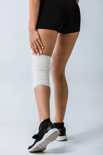 Vista ritagliata di sportiva con benda elastica sul ginocchio su grigio — Foto stock