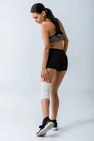 Full length view of sportswoman with elastic bandage on knee on grey — Stock Photo