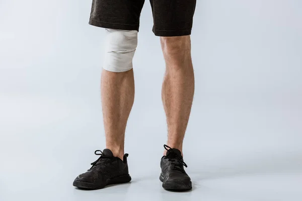 Cropped view of sportsman with elastic bandage on knee on grey — Stock Photo