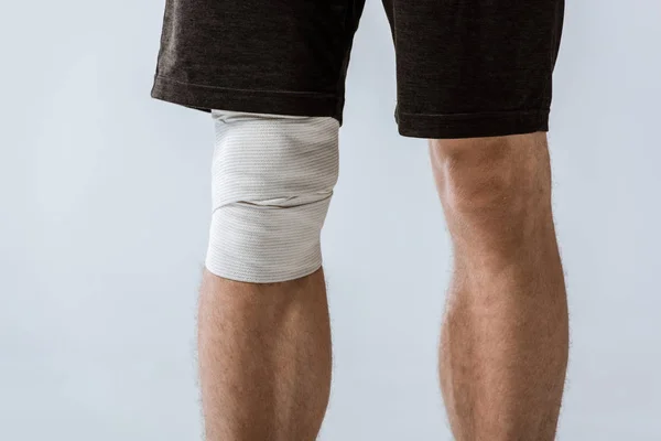 Abgeschnittene Ansicht des Sportlers mit elastischem Verband am Knie isoliert auf grau — Stockfoto